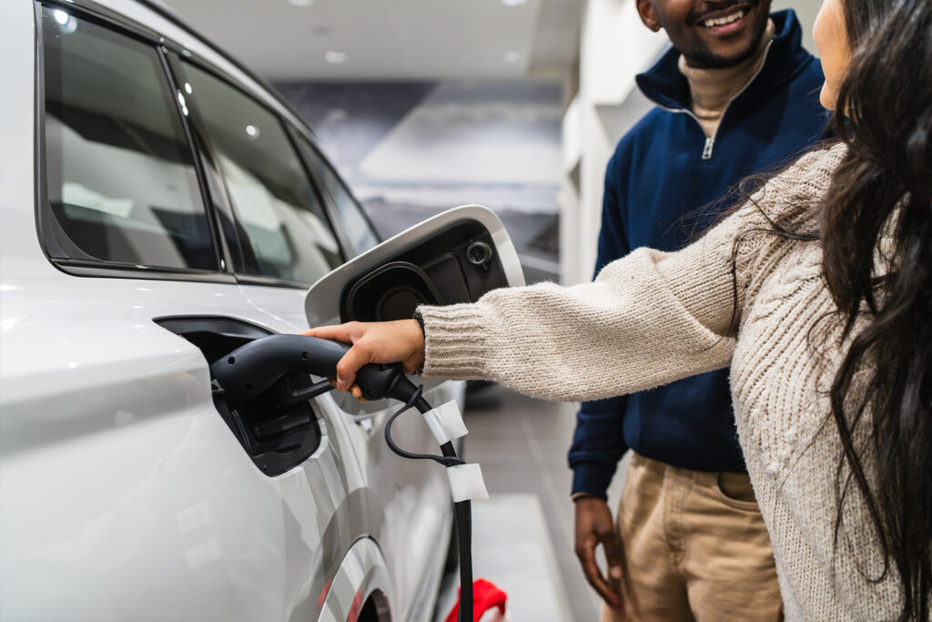 Two people looking at an electric vehicle on charge in a showroom, with one person holding the charging cable connected to the car.
