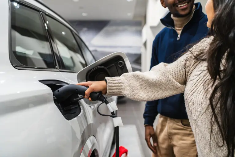Two people looking at an electric vehicle on charge in a showroom, with one person holding the charging cable connected to the car.